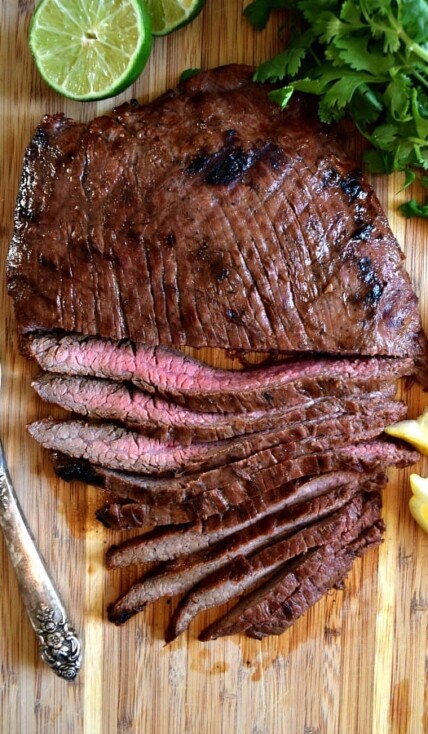 Overhead shot of grilled flank steak, half cut into strips showing off the pink meat inside