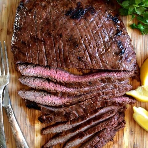 Overhead shot of grilled flank steak, half cut into strips showing off the pink meat inside