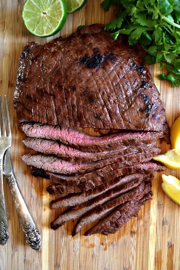 Overhead shot of grilled flank steak, half cut into strips showing off the pink meat inside