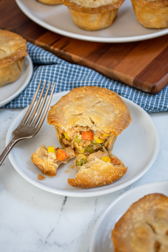 A mini turkey pot pie on a plate opened up by a fork to reveal the inside with leftover turkey and vegetables. 