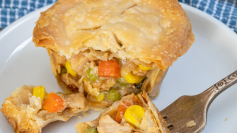 A fork with a bite of a mini leftover turkey pot pie on a small white plate.