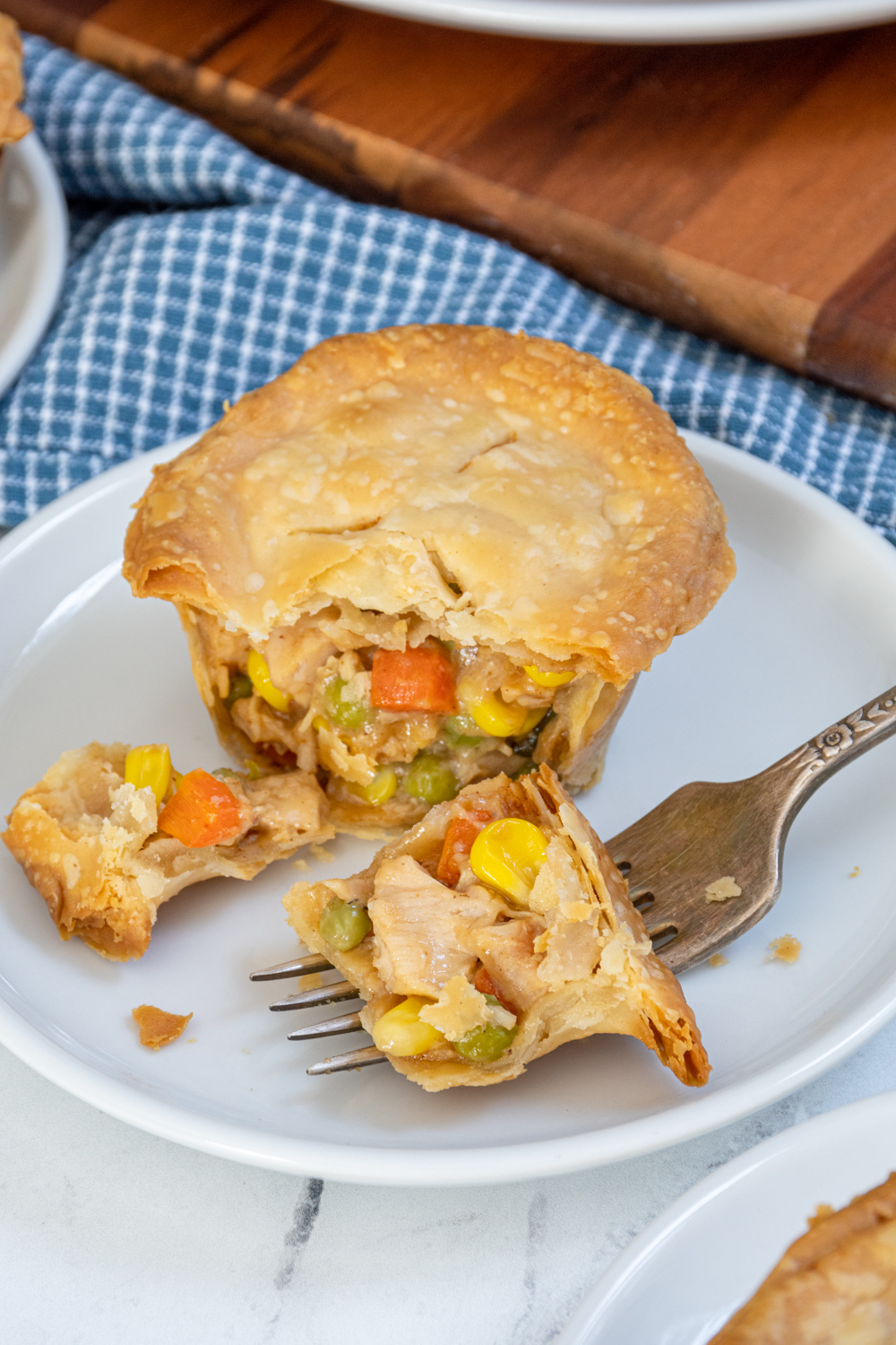 A fork with a bite of a mini leftover turkey pot pie on a small white plate.