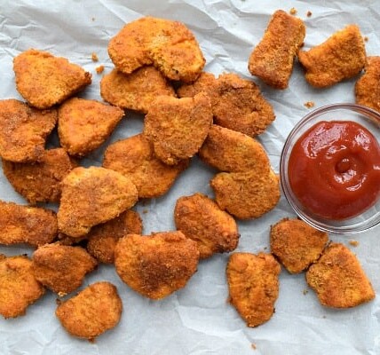 Baked Chicken Nuggets are spread out next to a bowl of ketchup