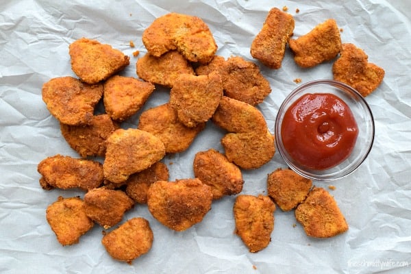 Baked Chicken Nuggets are spread out next to a bowl of ketchup