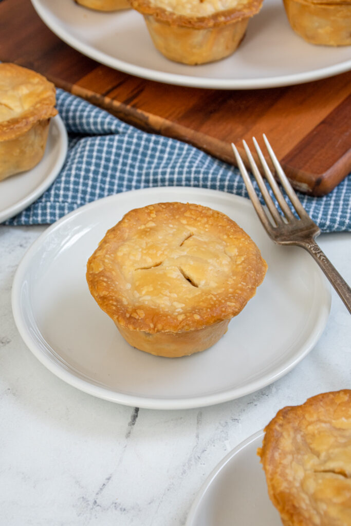 An individual mini leftover turkey pot pie on a small white plate next to a fork.