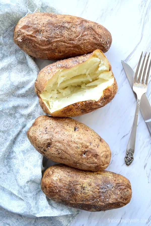 Perfect Baked Potatoes on a white tables with one cut open