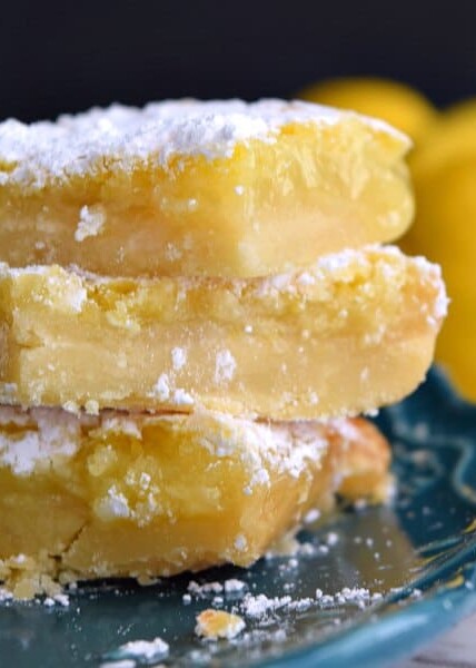 3 gooey lemon squares on a teal plate covered in powdered sugar