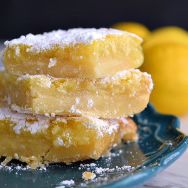 3 gooey lemon squares on a teal plate covered in powdered sugar
