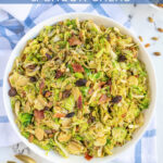 Pinterest Pin with text 'Warm Balsamic Brussel Sprout & Bacon Salad', image of a serving bowl full of shaved brussel sprout salad with bacon, raisins, and pumpkin seeds.