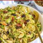 Pinterest Pin with text 'Warm Balsamic Brussel Sprout & Bacon Salad', image of a serving bowl full of shaved brussel sprout salad with bacon, raisins, and pumpkin seeds.