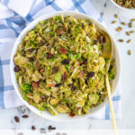 Pinterest Pin with text 'Warm Balsamic Brussel Sprout Salad', image of a serving bowl full of shaved brussel sprout salad with bacon, raisins, and pumpkin seeds.