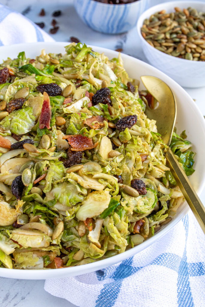 Close up of a bowl full of warm balsamic Brussel sprout salad garnished with bacon, raisins, and pumpkin seeds.