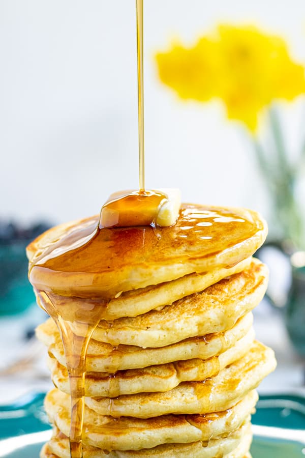 close up of maple syrup being poured onto a stack of pancakes