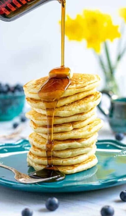 syrup being poured onto a tall stack of pancakes made from scratch