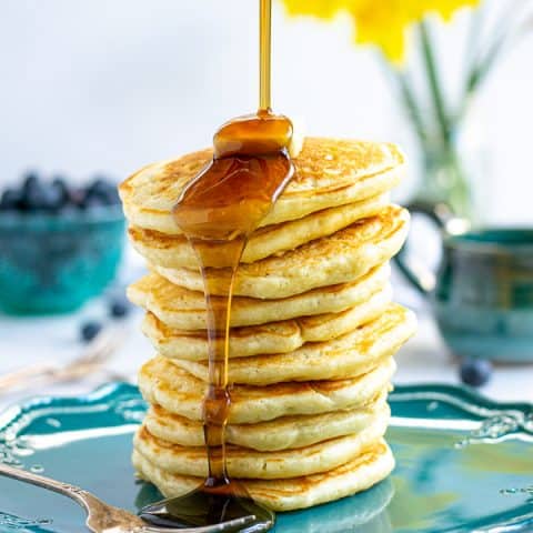 syrup being poured onto a tall stack of pancakes made from scratch