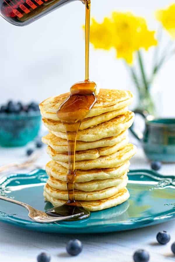 syrup being poured onto a tall stack of pancakes made from scratch