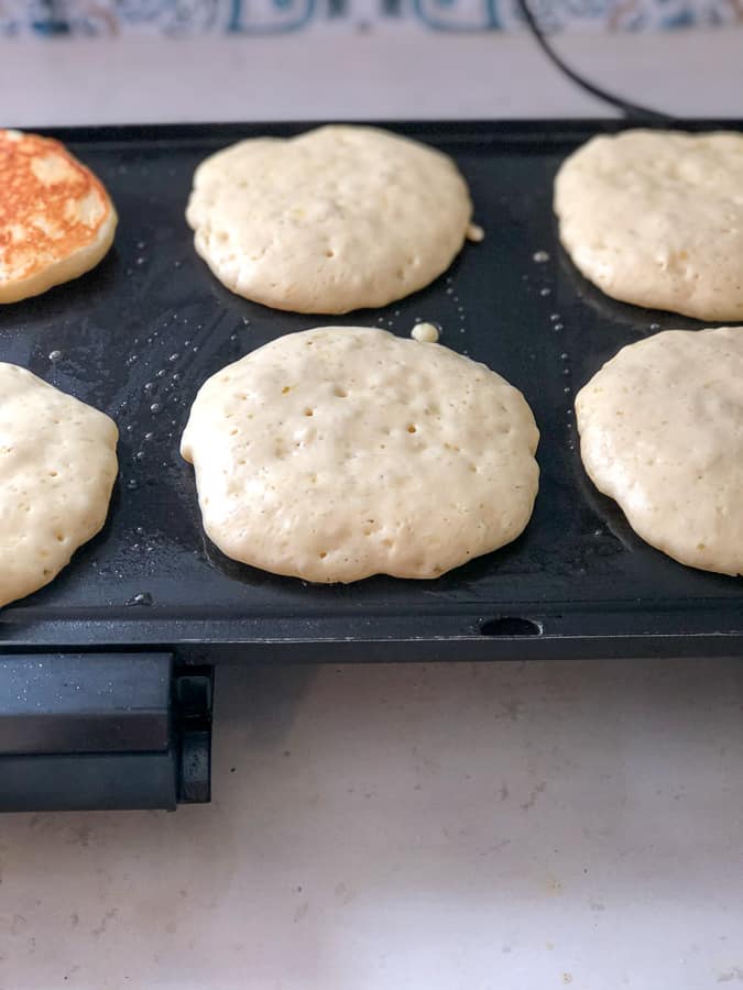 pancakes cooking on a griddle with air bubbles beginning to pop in the middle so you know when to flip the pancake