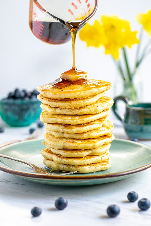 syrup being poured on a tall stack of fluffy pancakes