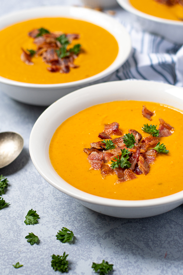 Close up of two bowls full of butternut squash soup garnished with bacon on a table.
