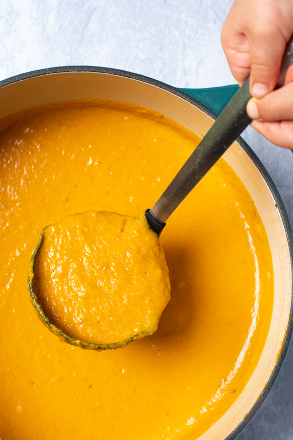 A ladle scooping butternut squash soup from a large pot.