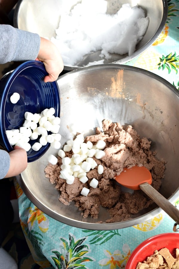 toddler hands adding mini marshmallows to snow ice cream