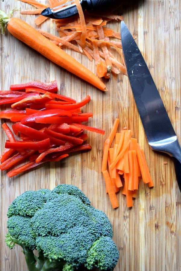 red bell pepper, carrots, and broccoli sitting on cutting board half cut up