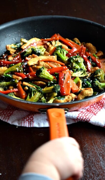 a toddler hand holding the handle of a skillet filled with 20 minute chicken stir fry
