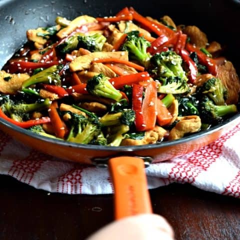a toddler hand holding the handle of a skillet filled with 20 minute chicken stir fry