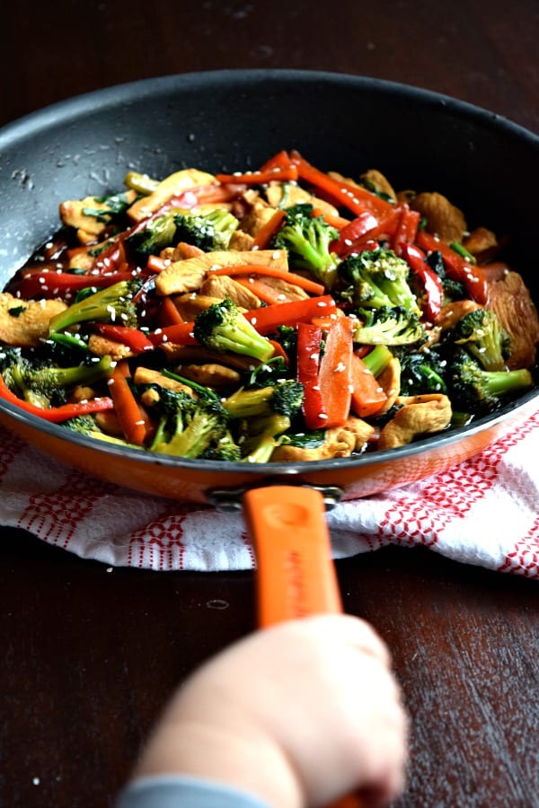 a toddler hand holding the handle of a skillet filled with 20 minute chicken stir fry