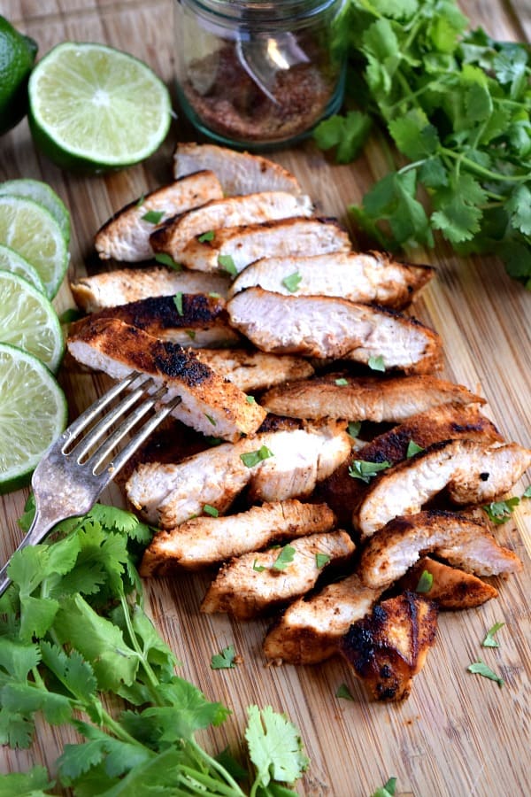 Southwest Chicken sliced and piled up on a cutting board with limes, cilantro, and a fork