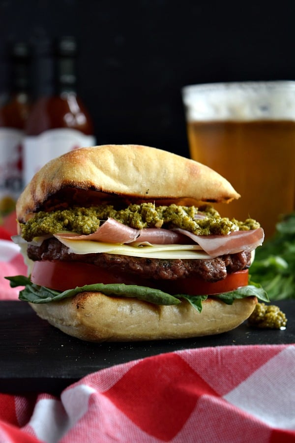 A prosciutto pesto burger on a black plate with a beer