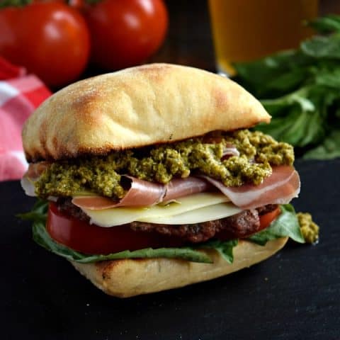 a close up of a prosciutto pesto burger on a black plate with a beer