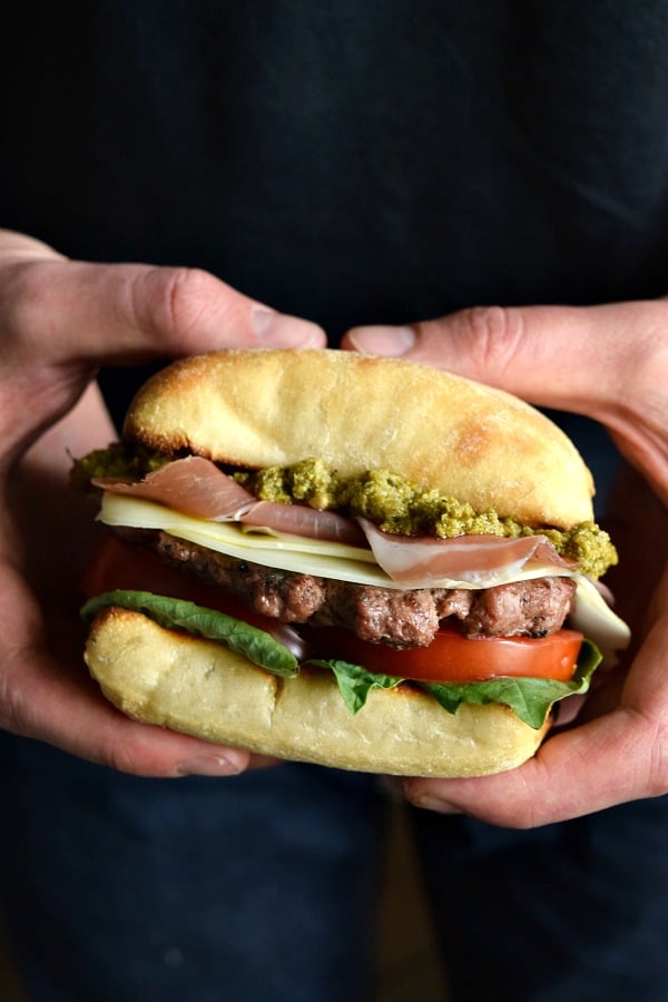 A Prosciutto Pesto Burger dripping with pesto in hands ready to be eaten