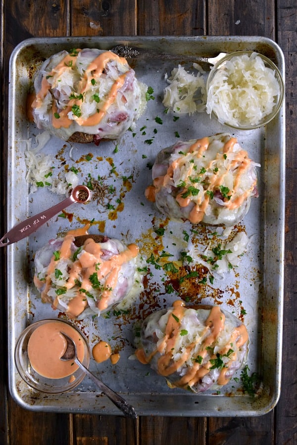 Reuben Stuffed Baked Potatoes on a sheet pan drizzled with a lot of 1,000 Island Dressing