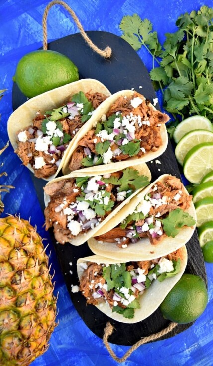 Slow Cooker Chipotle Pineapple Carnitas on a serving platter topped with cheese, onions, and cilantro