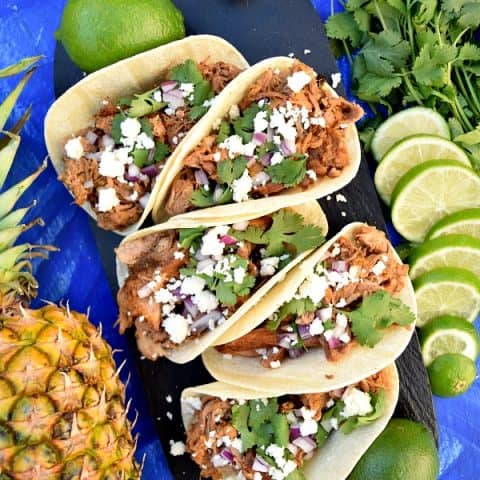 Slow Cooker Chipotle Pineapple Carnitas on a serving platter topped with cheese, onions, and cilantro