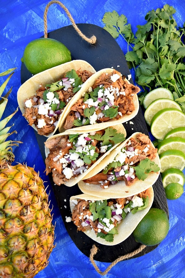 Slow Cooker Chipotle Pineapple Carnitas on a serving platter topped with cheese, onions, and cilantro