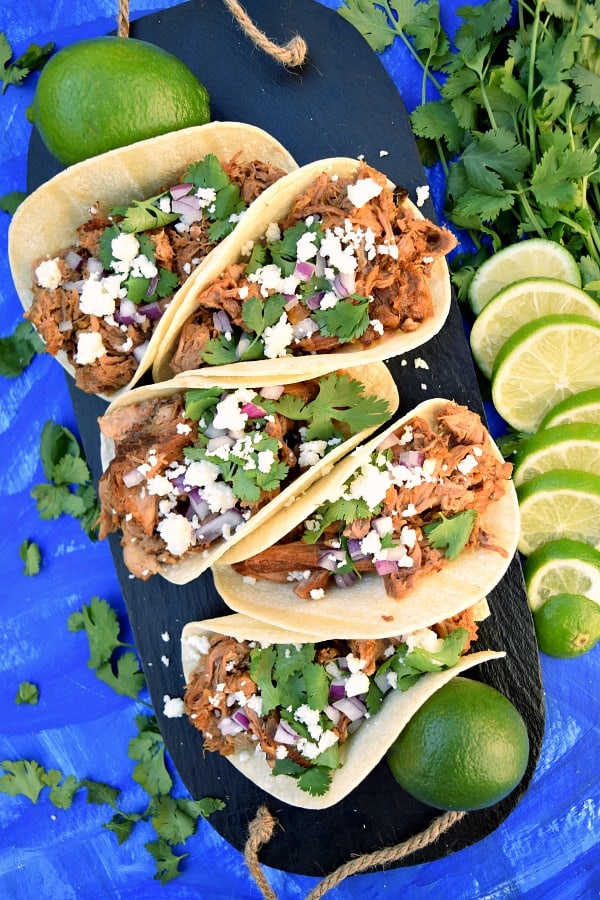 Slow Cooker Chipotle Pineapple Carnitas on a serving platter topped with queso fresco, diced red onion, and cilantro