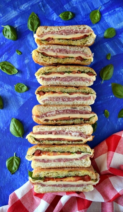 Italian Pressed Picnic Sandwich with a picnic napkin and basil leaves on a blue background