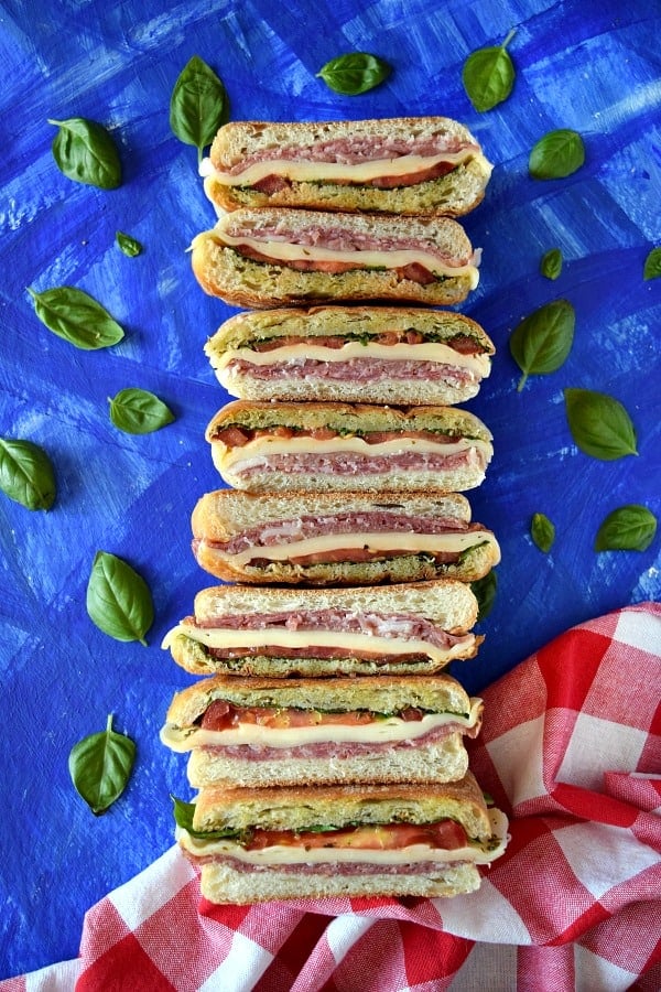 Italian Pressed Picnic Sandwich with a picnic napkin and basil leaves on a blue background