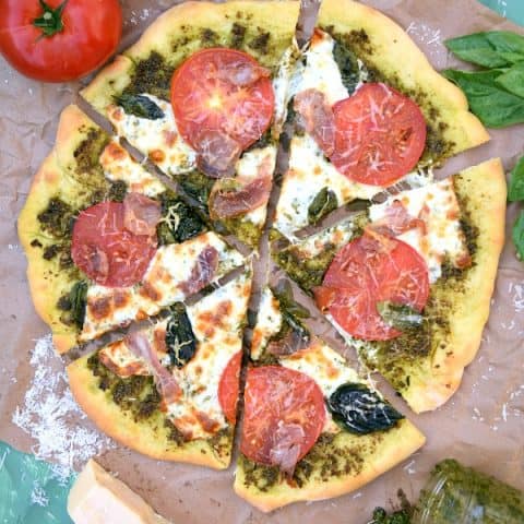 Pesto Pizza with Prosciutto, Tomatoes, and Mozzarella with 6 slices ready to be eaten