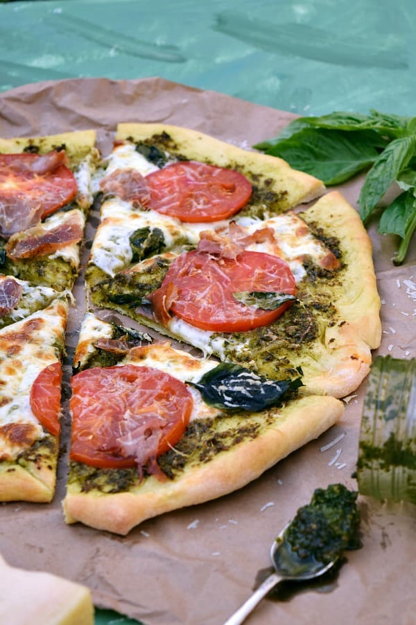 a close up shot of a few slices of Pesto Pizza with Prosciutto, Tomatoes, and Mozzarella