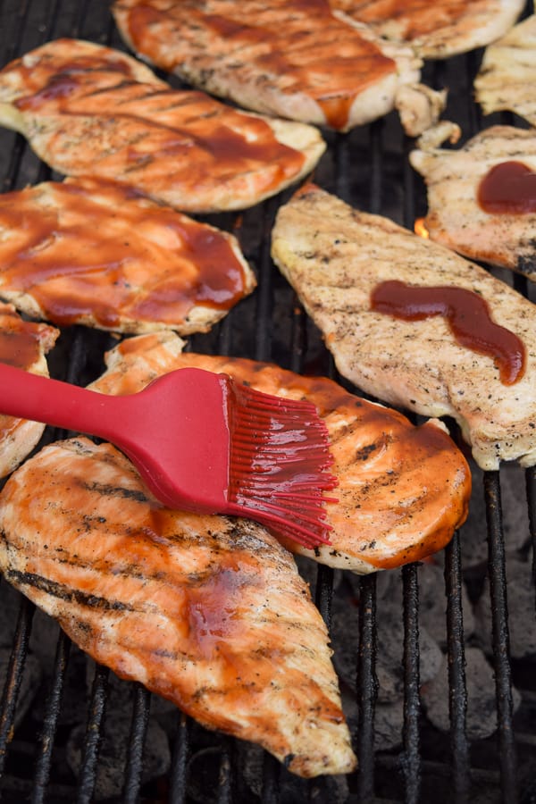 Barbecue being brushed onto a chicken breast on the grill