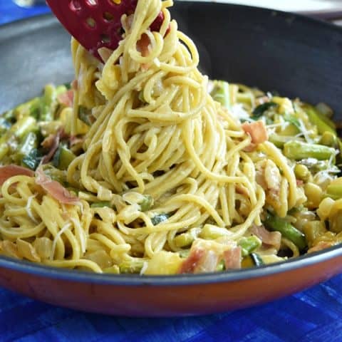 Summer Spaghetti Carbonara being pulled out of a large skillet showing the pasta covered in creamy carbonara sauce