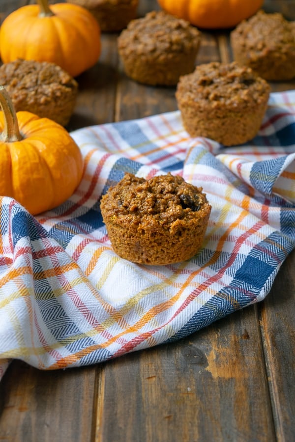 A Pumpkin Bran Muffin on a plaid towel with mini pumpkins
