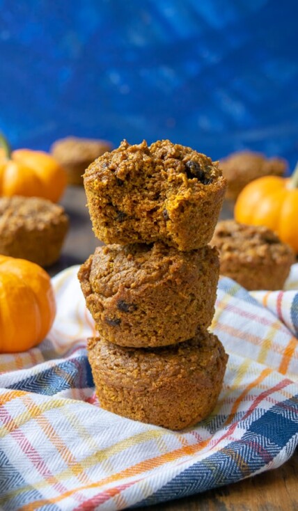Pumpkin Bran Muffins stacked on a plaid towel, the top one has a bite taken out