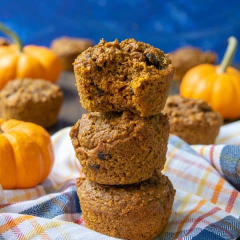 Pumpkin Bran Muffins stacked on a plaid towel, the top one has a bite taken out