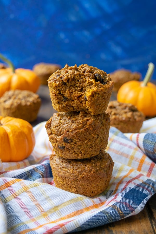 Pumpkin Bran Muffins stacked on a plaid towel, the top one has a bite taken out