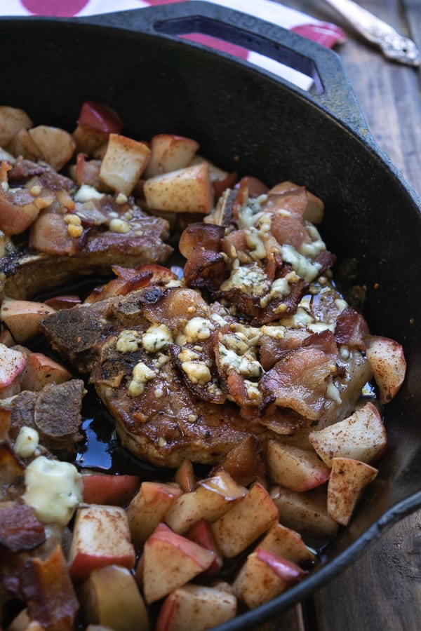 a pork chop in the cast iron skillet with crumbled bacon and melty cheese