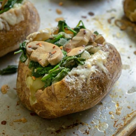 Spinach Mushroom Stuffed Baked Potatoes with Cheddar dripping down the side on a sheet pan